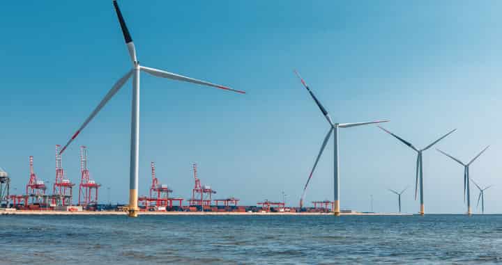 Wind turbines generating clean energy near a commercial shipping port, illustrating sustainable power generation and industrial development.